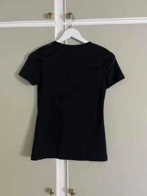 Svart Nike Dri-Fit t-shirt XS - Svart Nike Dri-Fit t-shirt i storlek XS med klassisk vit swoosh-logga på bröstet. T-shirten har rund hals och korta ärmar, tillverkad i ett lätt och funktionellt syntetmaterial som andas. Perfekt för dig som gillar sportig och clean stil.