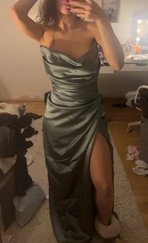 Grön satinklänning med slits - Säljer en lång, elegant grön klänning i satin som är strapless. Den har väldigt snygg figurnära passform som framhäver ens kurvor. Har bara använt den en gång, alltså den har inga skador. Den är från Jolie Bridal, vid köp av klänningen får man med sig deras tygpåse som skyddar klänningen. Priset kan diskuteras, om du har fler frågor om tex måtten så är det bara att skriva💕