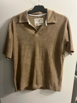Beige pikétröja Free Planet S - Säljer en beige pikétröja från Free Planet i storlek S. Tröjan har klassisk krage och korta ärmar, tillverkad i mjukt frottématerial som ger en chill och retro vibe. Perfekt för dig som gillar avslappnad stil med lite extra känsla.