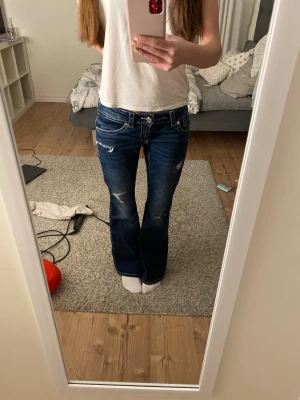 Blå bootcut jeans från Gina Tricot - Snygga mörkblå jeans från Gina Tricot i bootcut-modell med låg midja. Jeansen har slitna detaljer, kontrastsömmar och broderad bakficka💗