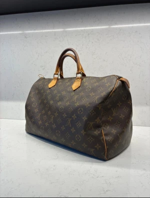 Louis Vuitton Speedy 35 Monogram - Louis Vuitton Speedy 35 i klassiskt monogrammönster. Som ni ser på bilderna har den vissa skavanker därav priset också. Den är självklart äkta och som ni ser finns serienumret inuti. Dragkedjan fungerar helt som vanligt inga konstigheter förutom att den trillat av och jag har säkrat den med en ring runt om. Finns något inuti väskan är osäker om det går bort men annars är den i fint skick förutom detta då. Tveka inte att höra av er :)