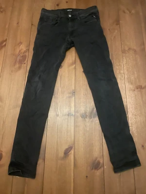 Svarta Replay Anbass jeans, stl 31/34 - Svarta jeans från Replay, modell Anbass. Slimmad passform med klassisk femficksdesign och diskret Replay-logga vid fickan. Jeansen är tillverkade i ett stretchigt bomullsmaterial som ger en bekväm känsla och snygg siluett.