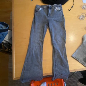 Grå bootcut jeans med utsvängda ben - Snygga grå jeans med bootcut-modell och utsvängda ben. Klassisk femficksdesign och normal passform. Jeansen är tillverkade i ett mjukt bomullsmaterial med en hint av stretch för extra komfort. Perfekta för dig som gillar en retroinspirerad look.