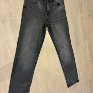 Grå regular fit jeans 170 från Jack & Jones - Snygga grå jeans från Jack & Jones i storlek 170, med klassisk femficksdesign och diskreta slitningar. Jeansen har smal passform och är tillverkade i stretchigt denim för extra komfort. Perfekta för dig som gillar en modern och enkel stil.