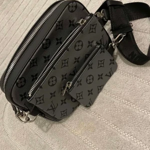 Svart axelväska monogram - Snygg svart axelväska med klassiskt monogrammönster. Väskan har flera fack med dragkedja och justerbar axelrem. Tillverkad i skinn med silverfärgade detaljer. Perfekt för dig som vill ha en stilren och praktisk väska.