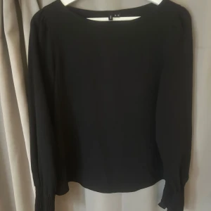 Svart blus med smockade ärmslut - Svart blus från Vero Moda  med rund halsringning och långa ärmar. Ärmsluten är smockade och har en lätt volangkant för en extra detalj. Super skön och fin 