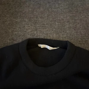 Svart stickad tröja från Lyle & Scott - Svart stickad tröja från Lyle & Scott med klassisk rund halsringning och gul logga. . Perfekt för dig som gillar stilren och enkel design.