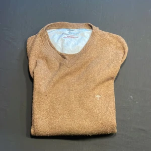 Brun v-ringad tröja Fynch-Hatton - Brun v-ringad tröja från Fynch-Hatton i en lyxig mix av merinoull och kashmir. Klassisk modell med ribbade muddar och diskret broderad logga på bröstet. Perfekt för dig som gillar stilrena och bekväma plagg med premiumkänsla.