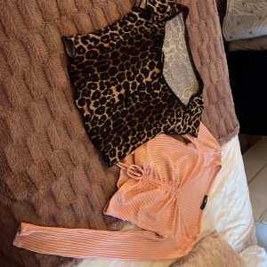 Leopardmönstrad mesh topp & rosa ribbad omlott - Säljer två snygga toppar! Ena är en croppad mesh topp med leopardmönster och svarta detaljer, perfekt för att sticka ut. Den andra är en ljusrosa ribbad omlottopp med långa ärmar och knyt framtill, mjuk och skön mot huden. Båda 30kr