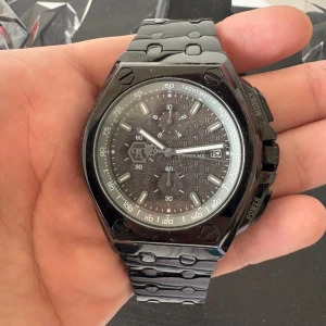 Svart klocka från Philipp Plein - Säljer en grymt snygg svart klocka från Philipp Plein med coolt geometriskt mönster på urtavlan och robust länkarmband i metall. Klockan har kronograf, tachymeter och levereras i en unik döskalleformad ask med PP-logga. Perfekt för dig som gillar statement-accessoarer. Ända problemet är att batteriet inte fungerar men kan lätt bytas ut, därav priset. Original pris är 4000 men priset kan sänkas vid snabb affär.