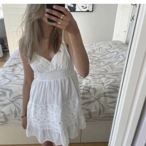 Vit somrig klänning med fint mönster - Superfin vit kort klänning med smala axelband, lite v-ringning och spetsdetaljer. Klänningen har smock i midjan och volang längst ner, perfekt för varma dagar, skolavslutning eller student. Lätt och luftig känsla, passar perfekt till sommaren.❤️