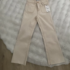 Beiga flare jeans från Zara, strl 34 - Snygga beiga jeans från Zara i modellen Mini Flare. Byxorna är högmidjade men samtidigt inte lågmidjade, utsvängda ben och ankellängd.  har klassiska fickor både fram och bak. Aldrig använd, prislappen finns kvar