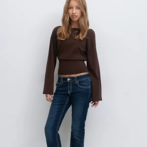 Brun tröja med v-ringad rygg gina 14+ - Snygg brun croppad tröja med lång ärm och v-ringad öppen rygg. Tröjan har en tight passform i midjan och vida ärmar. Perfekt för dig som vill ha en stilren men ändå unik look. Materialet känns mjukt och stretchigt. Aldrig använd och har prislappen kvar.