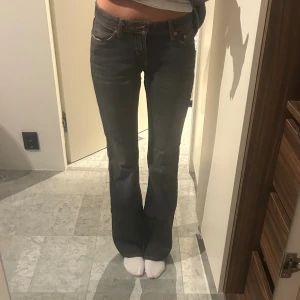  bootcut jeans mörkgrå - Snygga mörkgrå  jeans med bootcut passform och låg midja. Klassisk femficksmodell med subtila slitningar och orangea sömmar. Perfekta för dig som gillar en retro vibe och vill ha ett par jeans som sticker ut lite extra.