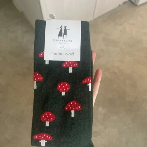 Svarta svampsockor från Bengt & Lotta - Svarta strumpor med röda och vita svampmotiv från Bengt & Lotta. Tillverkade i mjuk merinoull med inslag av polyamid och elastan för extra komfort. Perfekt för dig som gillar roliga detaljer och svensk design.