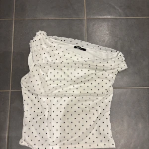 Prickig offshoulder topp från Gina Tricot - Snygg vit offshoulder topp från Gina Tricot med svarta prickar. Toppens ena axel är bar och tyget är lätt och stretchigt, perfekt för en trendig look. Passar dig som gillar att sticka ut med enkla men coola detaljer. Passar mig som brukar ha xs i Gina kläder och allmänt s endast använd 2 gånger 