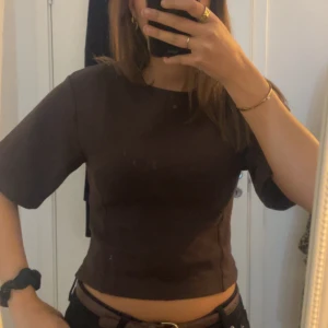 Brun croppad topp från Gina Tricot - Säljer en stilren brun croppad topp från Gina Tricot som är endast använd en gång. Toppen har rund halsringning och korta ärmar, med en enkel och clean design. Storlek L men känns som mer som  M. 