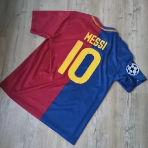 FC Barcelona Messi 10 Nike fotbollströja - Säljer en klassisk FC Barcelona fotbollströja med Messi 10 på ryggen. Tröjan är halva röd och halva blå, har korta ärmar och Champions League-märke på ärmen. Nike-logga och klubbmärke framtill, samt Unicef-tryck i gult. Perfekt för dig som älskar fotboll och Messi.