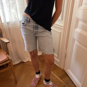 Ljusblå längre jeansshorts med slits - Säljer ett par ljusblå jeansshorts med råa kanter och slits på sidorna. Modellen är midwaist och har klassiska fem fickor samt dragkedja och knapp framtill. Perfekt för dig som gillar en loose och chill stil.