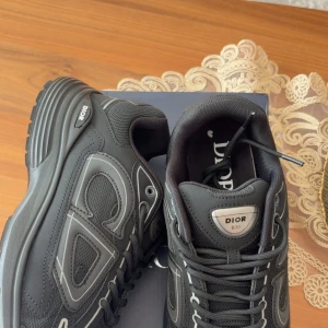 Svarta b3O sneakers - Säljer ett par svarta sneakers med coola reflekterande detaljer och tydlig på sidan. Skorna har snörning, meshpaneler och robust sula för en sportig vibe. Perfekta för dig som vill sticka ut med lyxig streetstyle.