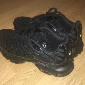 Nike Air Max Plus Tn helsvarta sneakers - Säljer ett par helsvarta Nike Air Max Plus Tn med klassisk Tn-detalj på hälen och sula. Skorna har en chunky sula med röda detaljer undertill, mesh och syntetmaterial på ovandelen samt snörning. Perfekta för dig som gillar streetwear och vill sticka ut.