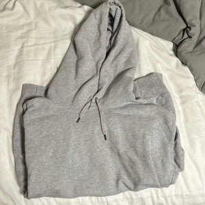 Grå hoodie från Uniqlo med huva - Säljer en stilren grå hoodie från Uniqlo i storlek L.  Sitter som M eventuellt STröjan har klassisk huva med snörning och är tillverkad i mjuk bomullsmix. Perfekt för chill dagar eller när du vill ha en enkel och clean look.