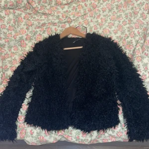 Svart pälsjacka från Gina Tricot - Säljer en svart fluffig pälsjacka från Gina Tricot i storlek M. Jackan har lång ärm, är helsvart och har en riktigt mjuk och lurvig känsla. Perfekt för dig som vill sticka ut med en cool och trendig look.