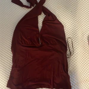 Vinröd omlott halterneck topp 157 - Snygg vinröd omlott halterneck topp från 157 The Black Label Collection. Toppen har djup v-ringning och knyt i nacken för en trendig look. Materialet är mjukt och har en lätt glans, perfekt för att sticka ut. Passar dig som gillar att klä dig stilrent och vågat.