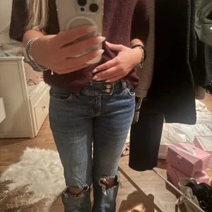 Jeans med hål - Säljer ett par blå jeans från 157 Paris Core med snygga slitningar och hål vid knäna. Klassisk femficksmodell med utsvängda ben och normal passform. Jeansen har låg midja och är tillverkade i robust denim för en cool vardagslook.