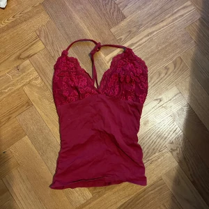 Vinröd spetsdetaljerad linnetopp - Säljer en vinröd linnetopp med spetsdetaljer och blommönster upptill. Toppen har smala axelband som knyts i nacken och en v-ringad hals. Materialet är mjukt och stretchigt, med spets i överdelen och slät bomull nedtill. Perfekt för dig som gillar romantiska vibes.