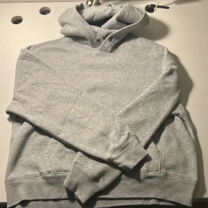 Grå hoodie från Hollister, Boxy Crop Fit - Säljer en ljusgrå hoodie från Hollister i boxy crop fit. Tröjan har huva, långa ärmar och en klassisk känguruficka framtill. Mjuk insida i fleece och ribbade muddar vid ärmslut och nederkant. Perfekt för chill dagar eller när du vill vara extra bekväm.