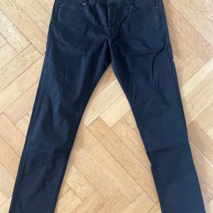 Svarta stretchjeans från Jack & Jones - Oanvända svarta jeans från Jack & Jones i storlek 33/32 med superstretch för extra komfort. Klassisk femficksmodell med smal passform och raka ben. Snygga och stilrena, perfekta till sneakers eller boots. Materialet är mjukt och följsamt för en modern look. 