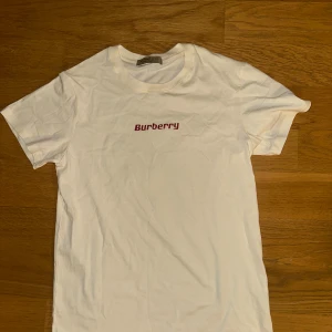 Beige Burberry t-shirt med röd ghost print - Beige t-shirt från Burberry med röd Burberry-logga på bröstet och ett stort rött ghost-tryck på ryggen. Klassisk rund hals och korta ärmar. Tillverkad i mjuk bomull för en skön känsla och clean look.