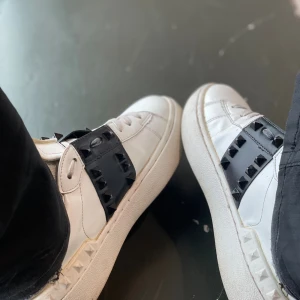 Valentino Rockstud sneakers vit/svart - Säljer ett par Valentino Rockstud sneakers i vitt skinn med svart band och ikoniska nitar. Snygg chunky sula och klassisk rund tå. Perfekta för dig som vill ha en statement-sneaker med lyxig känsla och coola detaljer. Säljer då dom har för små tyvärr.