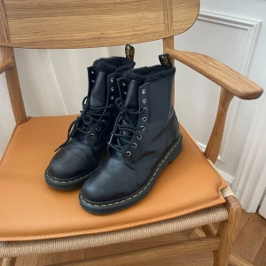 Svarta Dr. Martens med fluff - Säljer ett par svarta Dr. Martens i skinn med svart foder i pälsimitation. Klassisk gul söm runt sulan, grov yttersula och snörning framtill. Perfekta för kalla dagar.