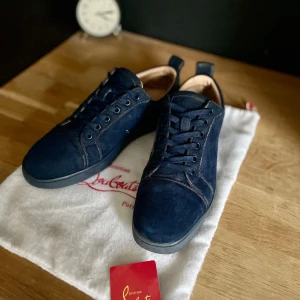 Christian Louboutin - Snygga mörkblå sneakers från Christian Louboutin i mjuk mocka med rund tå och platt sula. Skorna har ton-i-ton snörning, diskret broderad logga på hälen och lyxig läderinsida. Perfekta för dig som gillar exklusiva och stilrena sneakers.