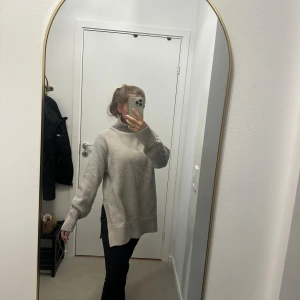 Beige stickad polotröja - Mysig beige stickad polotröja med ribbad hög krage och långa ärmar. Tröjan har en loose passform och slitsar i sidorna, perfekt för lager-på-lager. Enkel och stilren design som passar till det mesta.