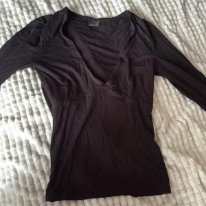 Svart långärmad v-ringad topp - Snygg svart långärmad topp med djup v-ringning och figurnära passform. Tillverkad i mjukt och stretchigt material som sitter skönt mot kroppen. Perfekt att styla med jeans eller kjol för en cool och enkel look.