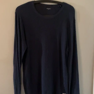 Mörkblå stickad tröja Jack & Jones - Mörkblå stickad tröja från Jack & Jones i storlek M. Tröjan har rund halsringning och långa ärmar. Perfekt för lager-på-lager och enkel att matcha med jeans eller chinos.