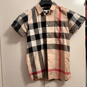 Burberry skjorta kortärmad  - Tja jag säljer en kortärmad burberry skjorta som har det ikoniska burberry mönstret på sig. Skjortan är i bra skick och är inte så värst använd. Jag säljer den för 500 vilket är ett bra pris i tanke på att en helt ny skjorta kostar 5000 ungefär men ni kan även pruta för den och skriv om ni har frågor. detta är en junior skjorta dock så i herrstorlek så blir det XS.