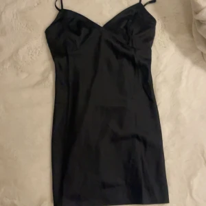Svart satin slipklänning - En svart, kort slipklänning i satin med smala axelband och v-ringad urringning. Använd en gång🩷