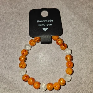 Handgjort armband  - Unikt handgjort armband med oranga melerade och vita krackelerade glaspärlo. Perfekt accessoar för dig som gillar färg och naturinspirerade smycken. Ca 16cm 