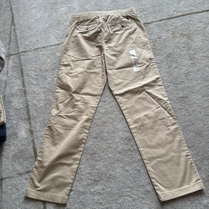 Beiga chinos, aldrig använda, från Polo Ralph Lauren - Snygga beiga chinos från Polo Ralph Lauren med rak passform och elastisk midja. Byxorna har klassiska fickor fram och bak, samt den ikoniska broderade loggan ovanför bakfickan. Aldrig använda. Klistermärke kvar. 