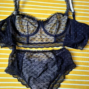 Svart prickig korsettopp i mesh - Säljer en svart korsettopp i transparent mesh med prickigt mönster och spetsdetaljer längs kanterna. Toppen har reglerbara axelband och bygel för extra stöd. Perfekt för dig som gillar en edgy och feminin stil.