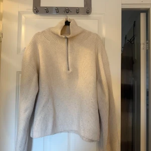 Beige stickad tröja med half zip - Säljer en beige stickad tröja med hög krage och half zip-dragkedja framtill. Tröjan har en loose passform och långa ärmar, perfekt för kyliga dagar. Enkel och stilren design som är lätt att matcha med olika outfits.