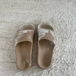 Beige Adidas Adilette sandaler - Säljer ett par beige Adidas Adilette sandaler med vit marmorering. De har en chunky sula och ribbad ovandel för extra komfort. Perfekta för sommaren och chill dagar. Adidas-logga på sidan. Tillverkade i syntetmaterial.
