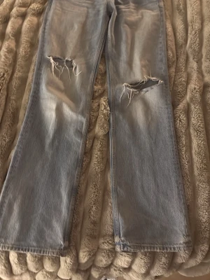 zara baggy jeans med hål - Snygga ljusblå jeans med raka ben och slitna detaljer vid knäna. Baggy jeans från zara knappast använda, säljer på grund av att dem sitter för tajt på mig i midjan och får ingen användning innerbensläng-84 midjemått rakt över-37