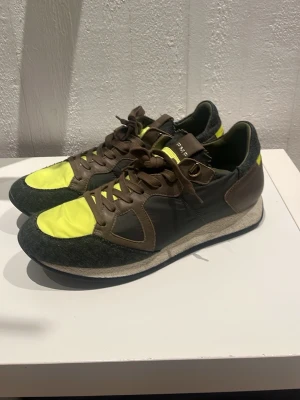 Sneakers från Philipe model i brun och neon - Snygga sneakers från Philipe model med brun mocka, detaljer i neon-gult tyg och mörkgrå partier. Skorna har snörning och en vit sula med svart yttersula. Perfekta för dig som vill sticka ut med färg och cool design! Pruta på!