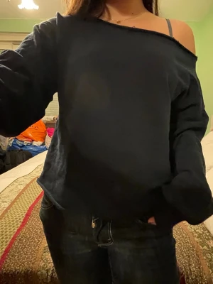 Mörkblå off shoulder sweatshirt - En mörkblå sweatshirt med off shoulder-design och avslappnad passform. Tröjan har långa ärmar och en bred halsringning som ger en trendig look. Perfekt att styla med jeans för en chill vibe.