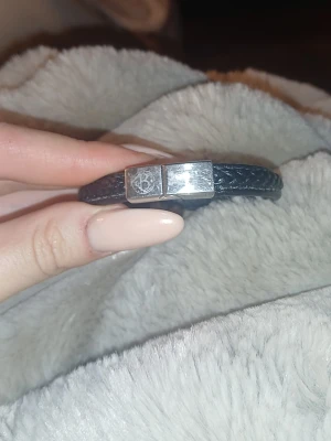 Svart flätat läderarmband med stålspänne - Snyggt svart armband i flätat läder med ett stilrent magnetlås i rostfritt stål. Spännet har en graverad logga som ger en exklusiv touch. Perfekt accessoar för dig som gillar en clean och modern look.